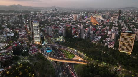 Aerial-view-overlooking-traffic-at-the-Petroleos-Fountain-and-intersection,-sundown-in-Mexico-city---reverse,-tilt,-drone-shot