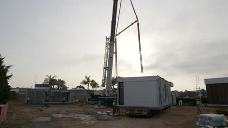 Construction-site-workers-using-crane-hoist-removing-modular-smart-home-unit-from-truck