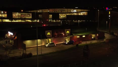 Vehicles-waiting-outside-McDonalds-fast-food-drive-through-illuminated-at-night-in-Northern-UK-town-aerial-orbiting-view