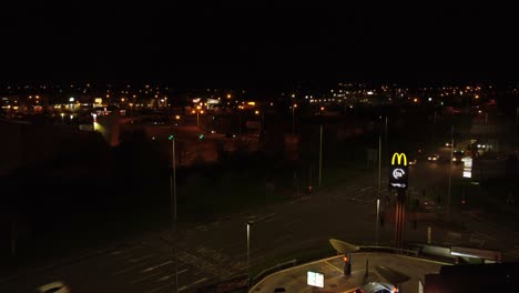 McDonalds-fast-food-drive-through-logo-illuminated-at-night-next-to-Northern-UK-town-highway-orbiting-aerial-view