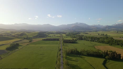 Aerial:-perfectly-straight-countryside-highway-leading-towards-majestic-mountain-range-in-warm-evening-sunshine