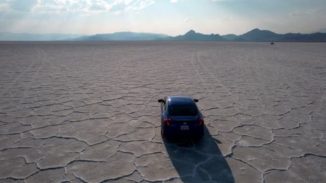 Aerial-following-shot-of-car-driving-on-endless-cracked-dry-bed-lake-in-Utah,Usa-during-sunny-day