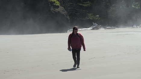 Woman-in-Red-jacket-Walking-in-Fog-and-Mist-on-Beach-with-Rock-Formations-in-Background