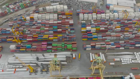 Rows-of-metal-containers,-windmills,-and-various-cargo-are-standing-in-the-container-terminal,-waiting-to-be-loaded-and-shipped-to-other-parts-of-the-world