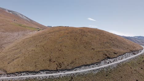 Aerial---narrow-dirt-road-leading-up-the-foothills-of-southern-alps-of-New-Zealand-on-a-sunny-spring-day
