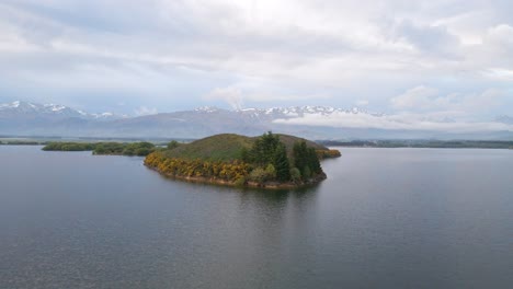 Drone-flight-over-lush-island-on-a-lake-and-southern-alps-of-New-Zealand-in-background