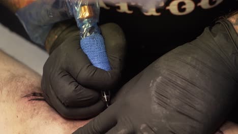 Tattoo-artist-his-hands-with-gloves-and-his-tattoo-machine,-coloring-the-skin-of-his-client