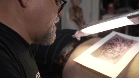 Tattoo-artist-putting-a-tattoo-on-a-man-his-arm-in-his-studio
