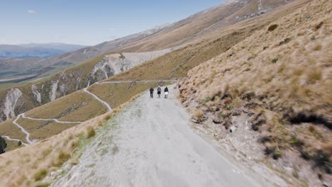 Hikers-walking-up-winding-dirt-road-on-the-side-of-a-mountain-covered-with-tussock-bushes