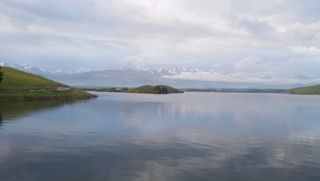Low-drone-flight-over-Lake-Opuha,-New-Zealand-with-snow-capped-mountains-in-background