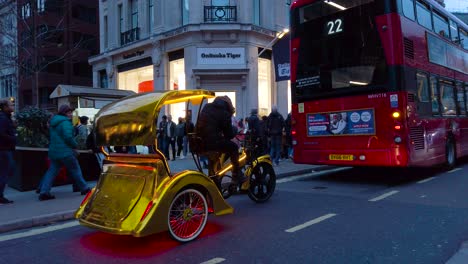 Shot-of-man-driving-a-golden-cycle-rickshaw-waiting-for-customers-along-the-roadside-in-London,-UK-at-daytime