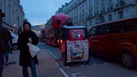 Following-shot-of-a-man-driving-his-rickshaw-tricycle-taxi-alongside-a-heavy-traffic-jam-in-the-street-of-London,-UK-during-evening-time