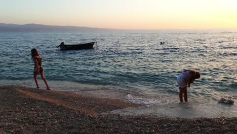 Children-running-through-the-water-in-the-sea-at-sunset,-backlit