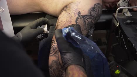 Man-getting-a-tattoo-on-his-upper-arm-over-shoulder-view