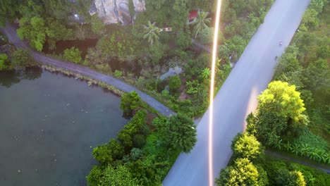 Luftaufnahme-Aus-Der-Vogelperspektive-Eines-Einzelnen-Gelben-Sonnenstrahls-über-Der-Straße-Und-Der-Tropischen-Landschaft-In-Ninh-Binh