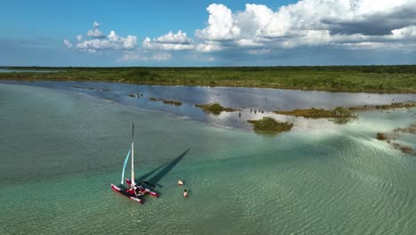 Aerial-view-around-a-small-sailboat-anchored-in-warm,-transparent-waters-of-the-Bacalar-Lagoon,-in-sunny-Mexico---orbit,-drone-shot