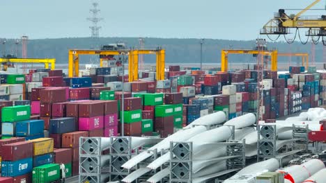 Rows-of-metal-containers,-windmills,-and-various-cargo-are-standing-in-the-container-terminal,-waiting-to-be-loaded-and-shipped-to-other-parts-of-the-world