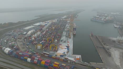 Aerial-view-of-the-port-area's-container-terminal,-metal-containers-with-cargo,-and-ships-moored-at-the-quays-in-the-early-and-dark-morning-in-Klaipeda-port
