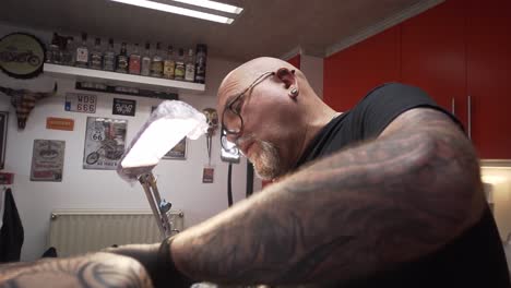 Tattoo-artist-with-beard-and-glasses-tattooing-in-his-studio
