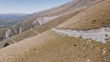 Tussock-grass-covered-mountain-side-with-a-narrow-dirt-road-leading-up-in-Mackenzie,-New-Zealand