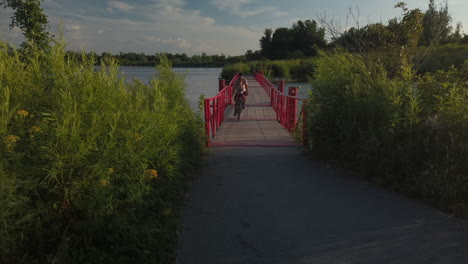 Exterior-wide-shot-of-cycling-duo-crossing-the-red-floating-bridge-at-Tommy-Thompson-Park