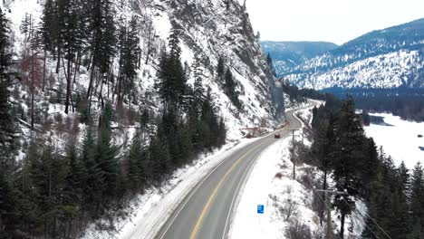 Eine-Folgeperspektive-Eines-Roten-Autos-Auf-Dem-Yellowhead-Highway-5-Durch-Das-Gefrorene-North-Thompson-River-Valley-In-Der-Nähe-Von-Kamloops,-Atemberaubende-Bergige,-Schneebedeckte-Landschaft