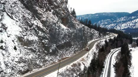 A-Semi-Truck-Hauling-a-Boat-Across-a-Cold-Highway-5-in-the-North-Thompson-River-Valley-Near-Kamloops,-with-a-Tight-Road-and-Protected-Rockface-Alongside