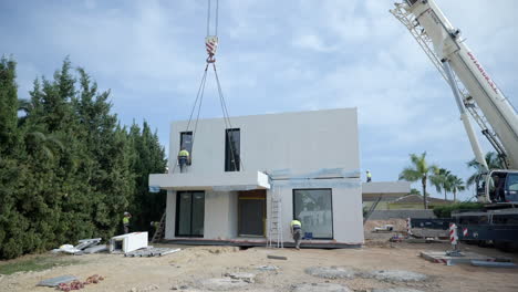 Workers-installing-modern-modular-smart-home-development-suspended-by-crane-on-real-estate