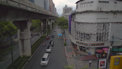 Cars-and-a-tuk-tuk-driving-on-road-next-to-elevated-train