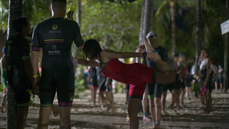 Male-and-female-athletes-wearing-swimwear-warming-stretching-and-preparing-for-the-start-of-the-swimming-stage-of-a-triathlon-on-the-beach