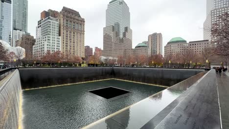 Ground-Zero-at-the-National-September-11-Memorial-and-Museum-911-Memorial-and-Museum---tilt-up-to-reveal-the-New-York-City-skyline-on-rainy-cloudy-day