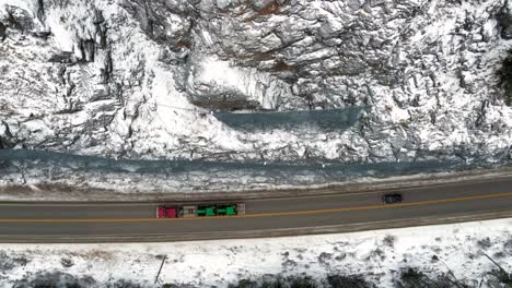 Overhead-Shot-of-an-red-Semi-Truck-Hauling-Green-Tractors-on-Highway-5-in-the-North-Thompson-River-Valley-Near-Kamloops-along-a-Tight-Road-and-Protected-Rockfaceside