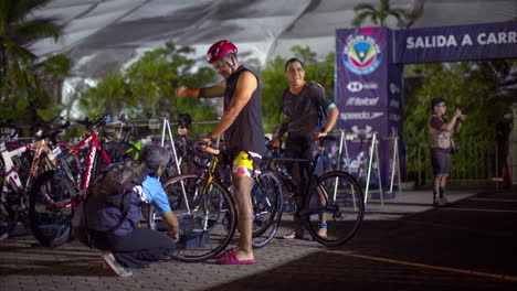 Atleta-Inspeccionando-Los-Neumáticos-De-Su-Bicicleta-Antes-De-Que-Comience-La-Competencia-De-Triatlón-Usando-Traje-De-Baño-Y-Casco