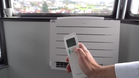 Holding-up-remote-and-turning-down-temperature-on-heat-pump-seen-in-background---Male-arm-in-first-person-reducing-energy-cost---Daikin-heat-pump