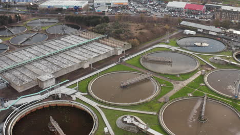 Aerial-shot-rotates-around-a-sewage-plant-with-hundreds-or-seagulls-circling-and-an-industrial-estate-in-the-background