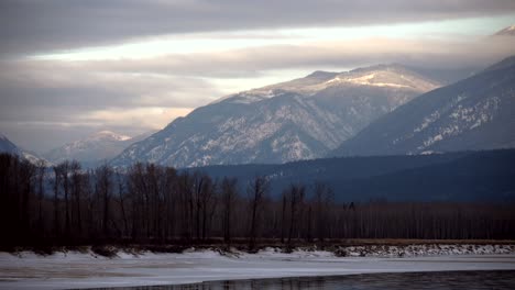 Time-Lapse-of-Thick-Clouds-in-Golden-Hour-Light-Over-Snowy-Peaks-and-the-Frozen-North-Thompson-River-Near-Little-Fort,-BC