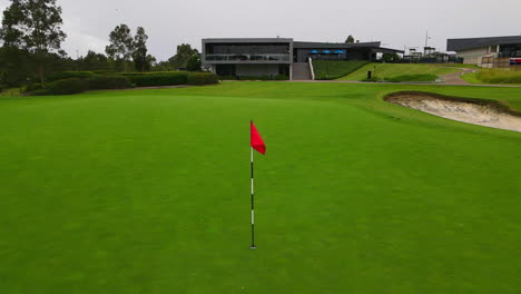 red-golf-pole-flag-on-manicured-green-at-golf-course-with-bunker-Pt-2