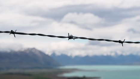 Close-up-of-barbed-wire-fence-with-turquoise-lake-and-stunning-mountain-scenery-in-background