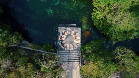Top-down-aerial-view-of-people-doing-yoga-on-a-deck-at-the-Cenote-in-Tulum,-Mexico