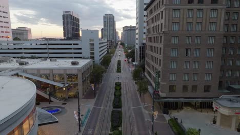 Aerial-view-through-the-main-street,-passing-the-downtown-Greenstreet-in-Houston,-sunrise-in-Texas,-USA