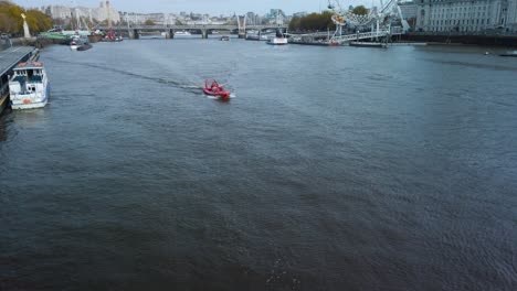 Toma-Aérea-De-Un-Barco-Rojo-Navegando-En-El-Río-Támesis,-Londres,-Gran-Bretaña.