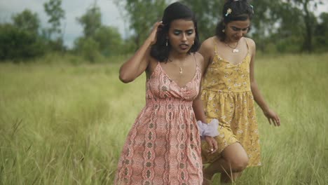 Two-attractive-Asian-females-enjoying-each-other's-company-happily-laughing-and-smiling-as-they-walk-through-a-grassy-field-enjoying-being-outdoors-in-nature,-India