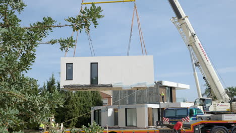 Contemporary-modular-smart-home-unit-hanging-over-foundation-site-by-crane-lift