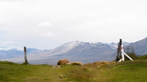 Fence-posts-on-green-meadow-on-windy-day-in-New-Zealand-with-stunning-mountains-in-background