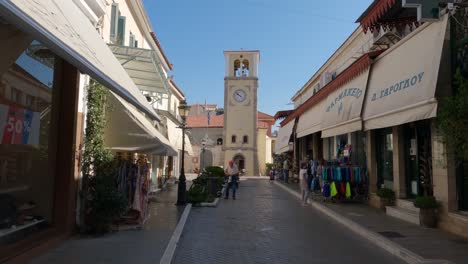 Calle-Con-Tiendas-Y-Vista-Hacia-La-Torre-Del-Reloj-Veneciano-De-Preveza,-Grecia