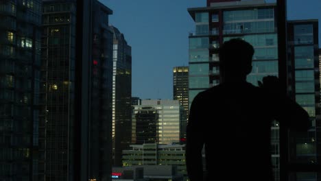 Man-in-deep-thought-overlooking-the-city-with-skyscrapers,-during-blue-hour-at-dusk