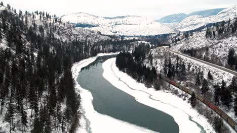 Winter-Journey:-Freight-Train-Navigates-Through-a-Snowy-Canyon-in-British-Columbia's-North-Thompson-River-and-Yellowhead-Highway-5-Near-Kamloops,-Aerial-Shot-Follows