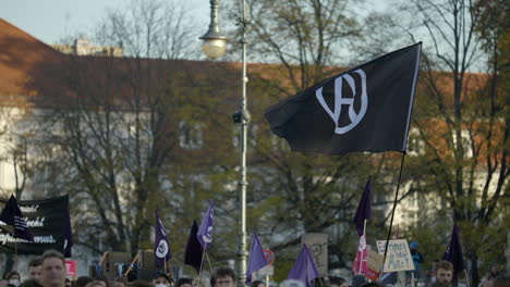 Black-anarchy-flag-waving-above-Berlin-crowd-protesting-economic-inflation-situation,-Slow-motion