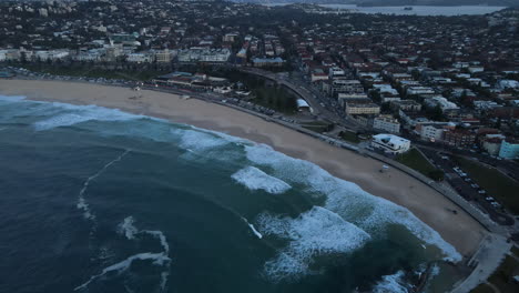 High-Drone-shot-along-Bondi-beach-with-waves-lapping-and-clear-beach