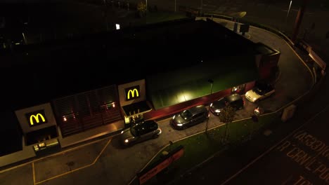 Flying-over-cars-waiting-at-McDonalds-fast-food-drive-through-at-night-aerial-view